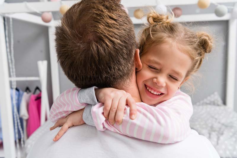 Smiling young girl hugging her father, symbolizing joyful parental reunification.
